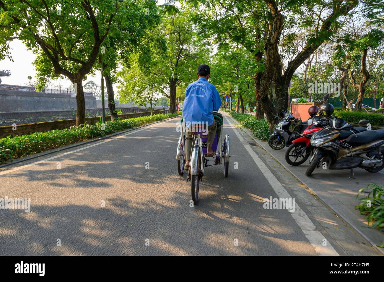 Un ciclista di taxi triciclo pedala lungo le strade della città di Hue, in Vietnam. Foto Stock