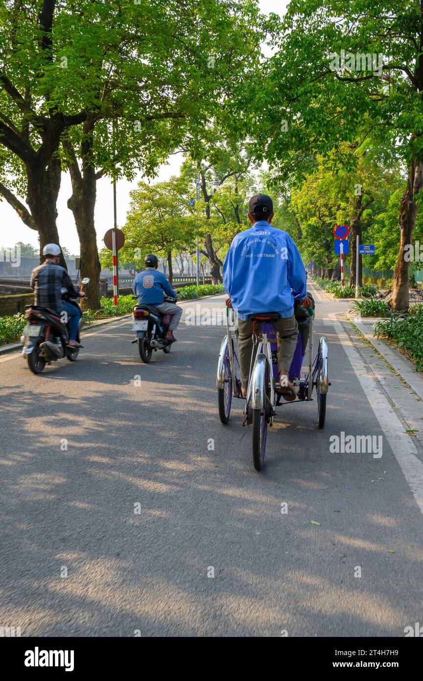 Un ciclista di taxi triciclo pedala lungo le strade della città di Hue, in Vietnam. Foto Stock