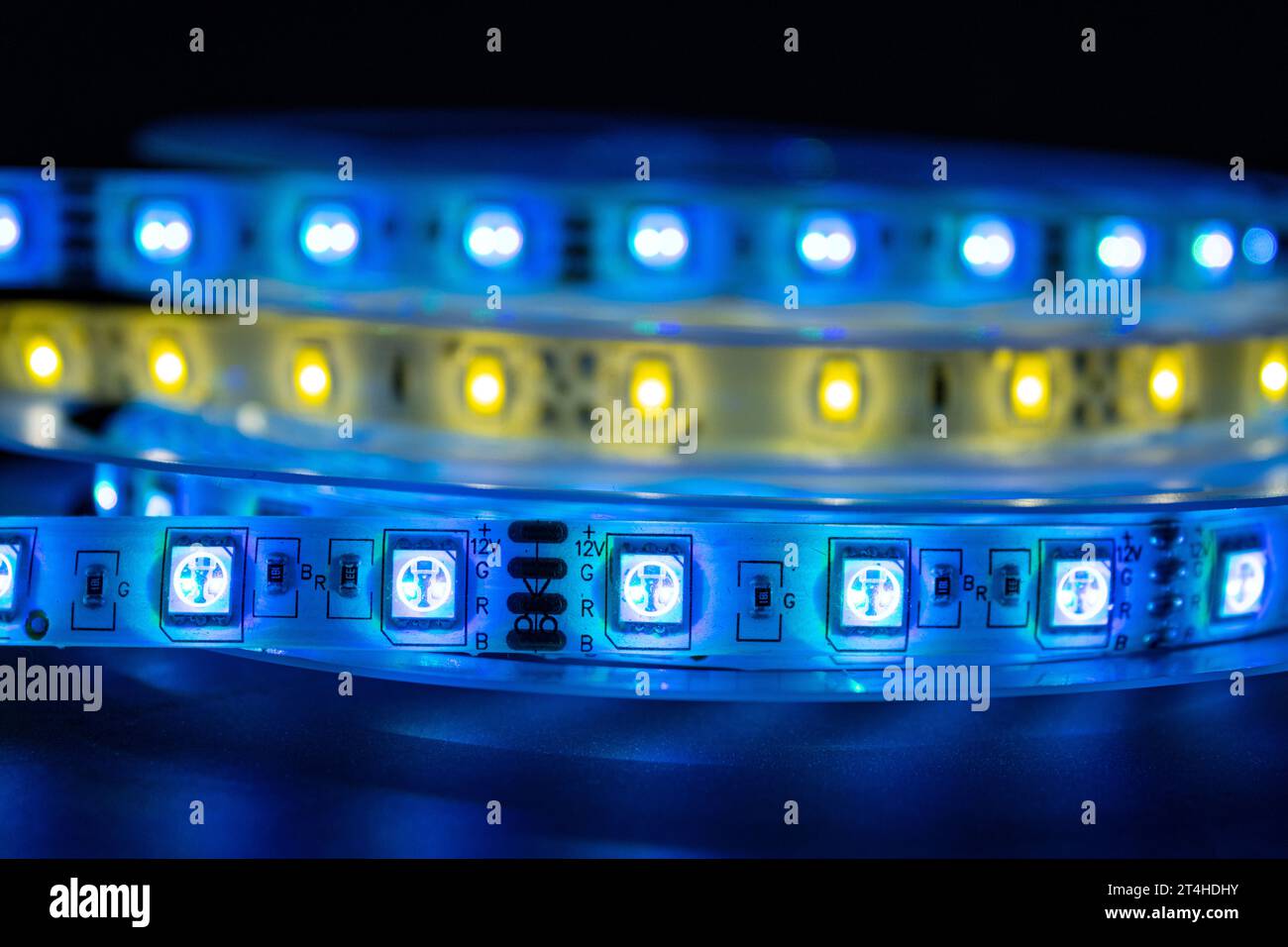 Bobina con rotolo di strisce luminose LED luminose posizionate sul tavolo, colore blu e bianco caldo nelle stanze buie Foto Stock