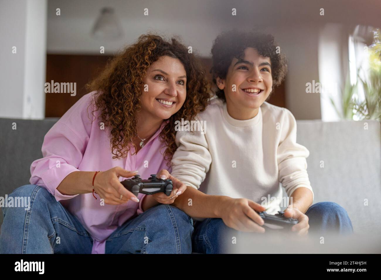 Madre e figlio che giocano ai videogiochi mentre sono seduti sul divano a casa Foto Stock