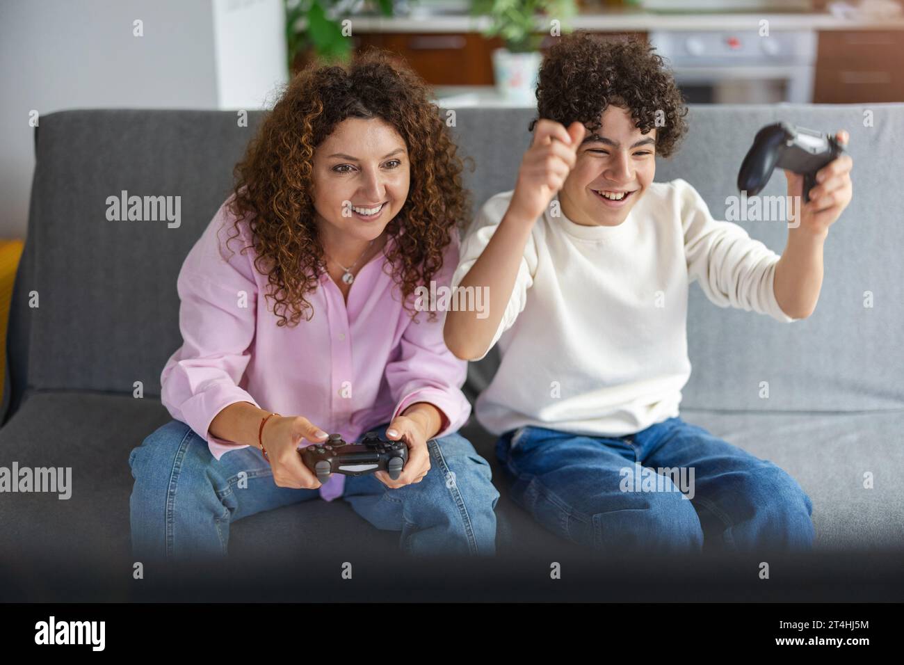 Madre e figlio che giocano ai videogiochi mentre sono seduti sul divano a casa Foto Stock