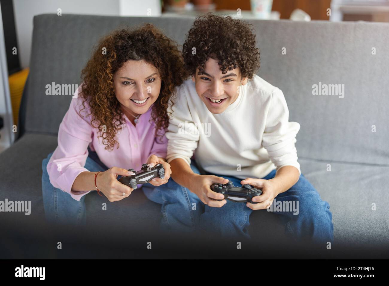 Madre e figlio che giocano ai videogiochi mentre sono seduti sul divano a casa Foto Stock