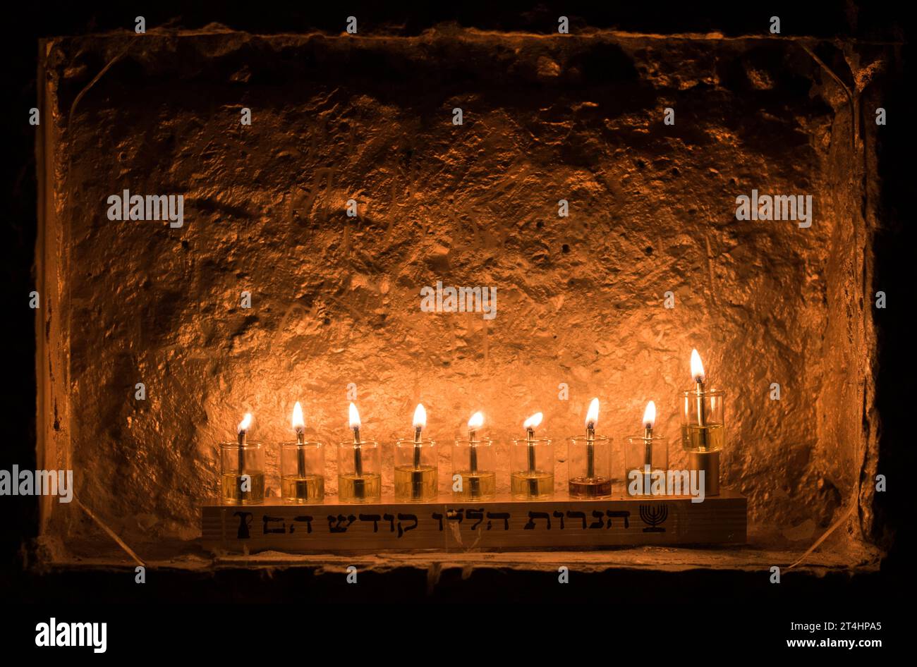 Una menorah Hanukkah con le parole ebraiche "queste candele sono Sacre" alla base e fiale di vetro di olio e stoppini brucianti che riflettono una luce brillante di Foto Stock