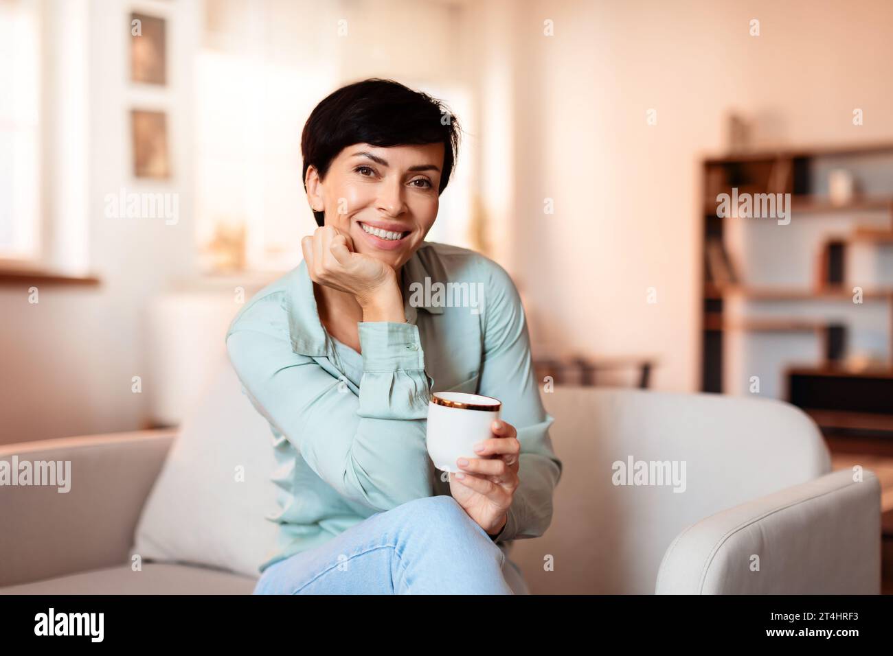 Allegra signora di mezza età che si rilassa e si gusta il caffè al chiuso Foto Stock