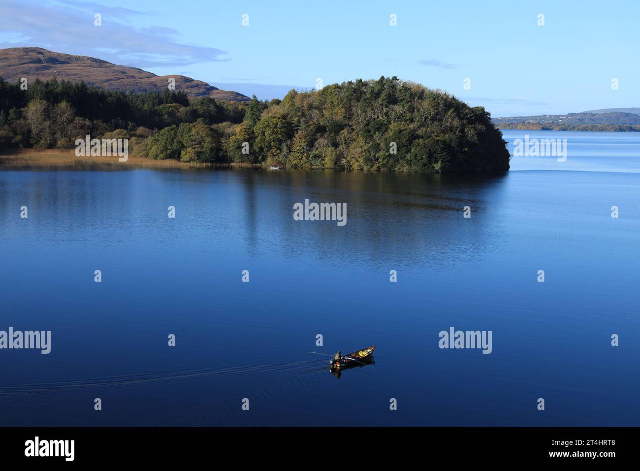 Paesaggio a Lough Gill, contea di Leitrim e contea di Sligo, Irlanda, con l'uomo che pesca da una piccola barca in acque ancora riflettenti il giorno autunnale Foto Stock