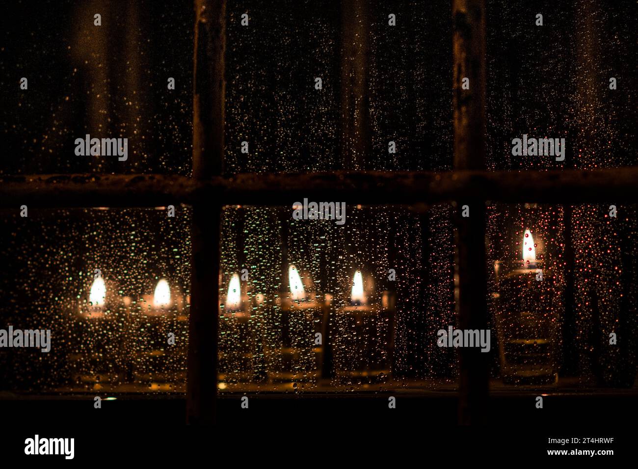 Fiale di olio e stoppini brucianti in una menorah brillano brillantemente in una finestra in una notte di pioggia a Gerusalemme durante il festival ebraico di Hanukkah. Foto Stock