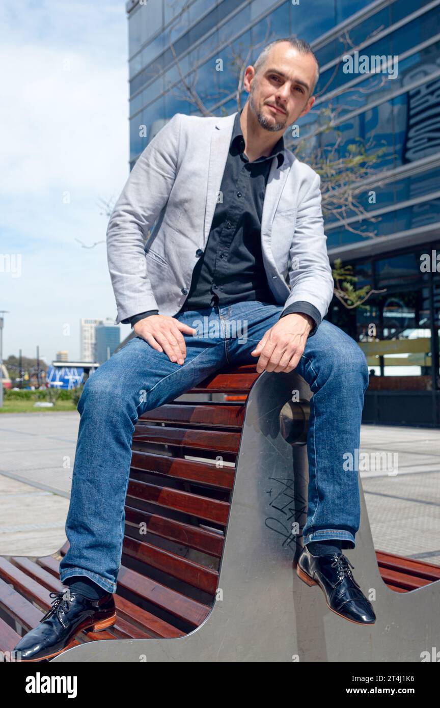 Ritratto verticale di un uomo d'affari caucasico adulto con barba, capelli corti e cappotto grigio, in posa all'aperto all'esterno degli edifici di lavoro al noo Foto Stock