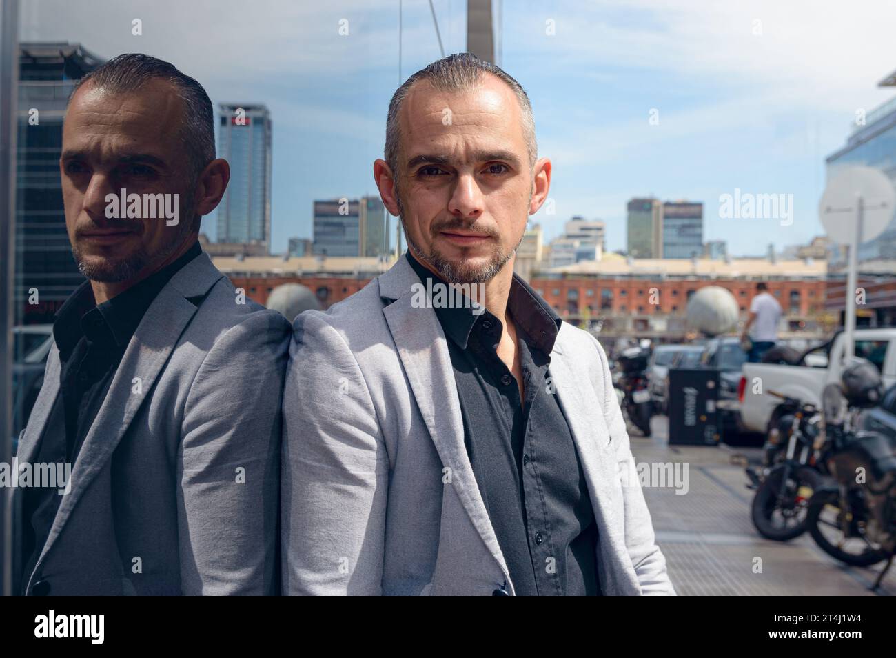 Ritratto di un uomo d'affari caucasico adulto, con giacca, capelli corti e barba, all'aperto appoggiato contro una parete di vetro, in posa Foto Stock