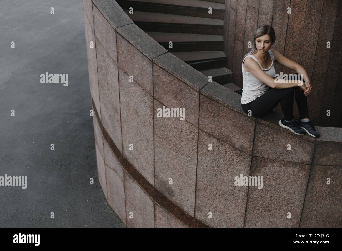Ritratto di una giovane donna sportiva del parkour. Atleta freeruning seduta a muro. Foto Stock