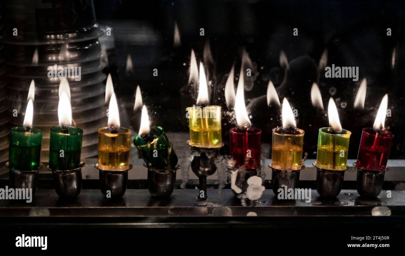 Le fiale di vetro multicolore contengono olio e stoppini brucianti in una menorah luminosa nell'ottava notte del festival ebraico di Hanukkah. Foto Stock