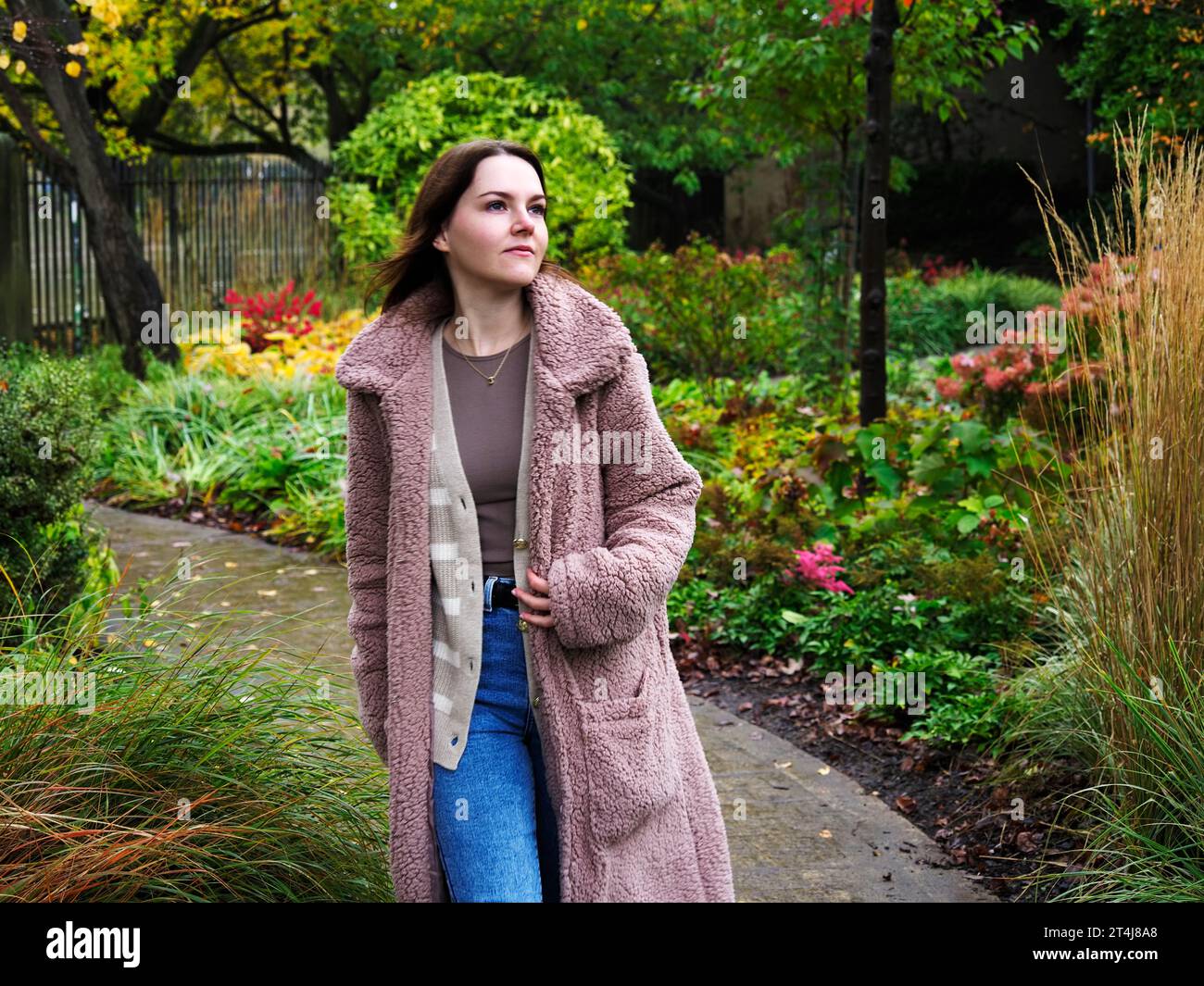 Giovane donna con i capelli castani delle spalle che cammina lungo un sentiero in una giornata autunnale nei giardini di York, Yorkshire, Inghilterra Foto Stock