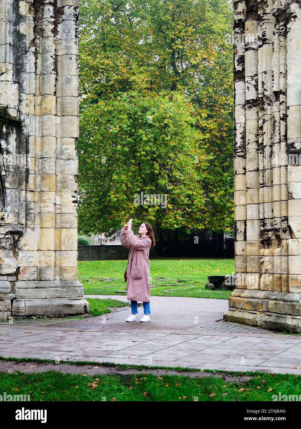 Giovane donna che scatta fotografie con uno smartphone in una giornata autunnale al Museum Gardens di York, Yorkshire, Inghilterra Foto Stock