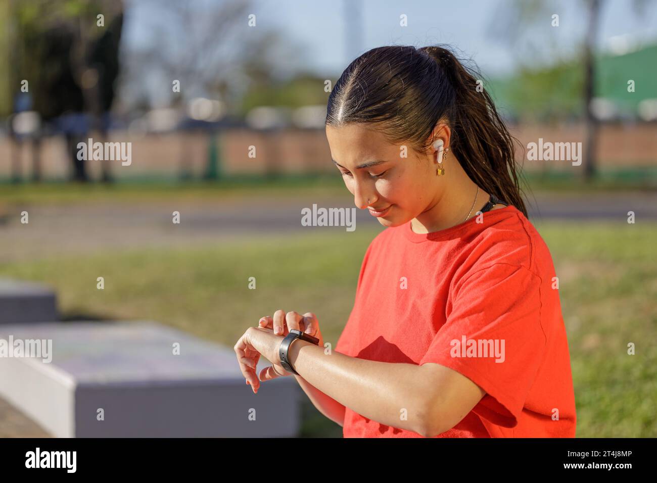 Ragazza latina con maglietta rossa che controlla il suo orologio intelligente. Foto Stock