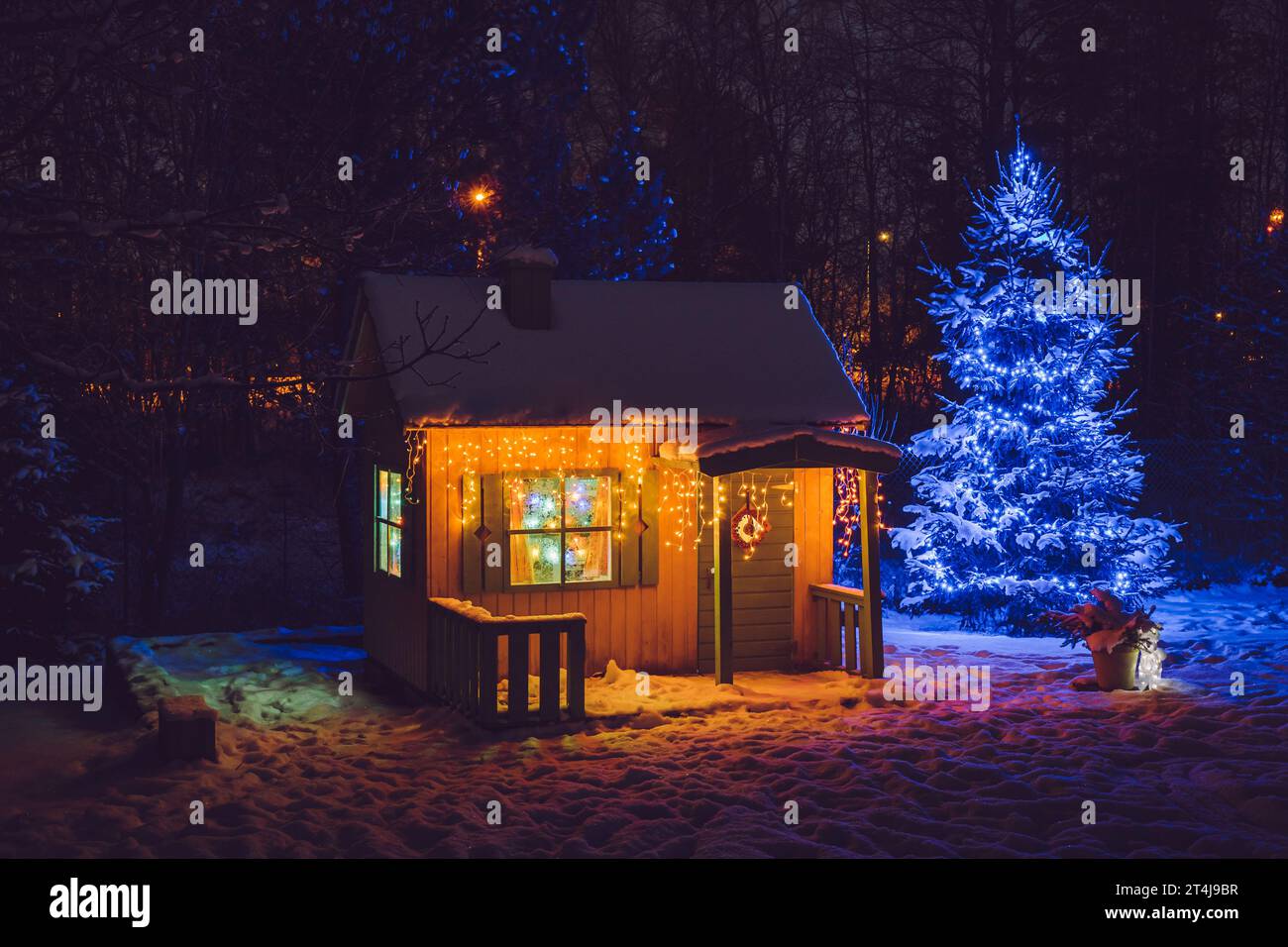 Casa da gioco privata per bambini in legno dipinto di giallo nel giardino domestico, decorata con luci a LED di Natale all'aperto in una notte fredda. Foto Stock