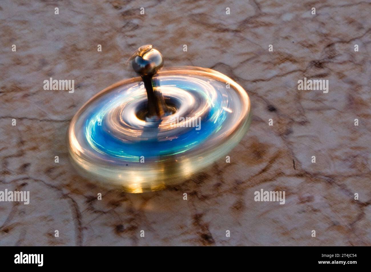 Piccolo dreidel Hanukkah in vetro blu e oro che gira in movimento su un muro di pietra. Foto Stock