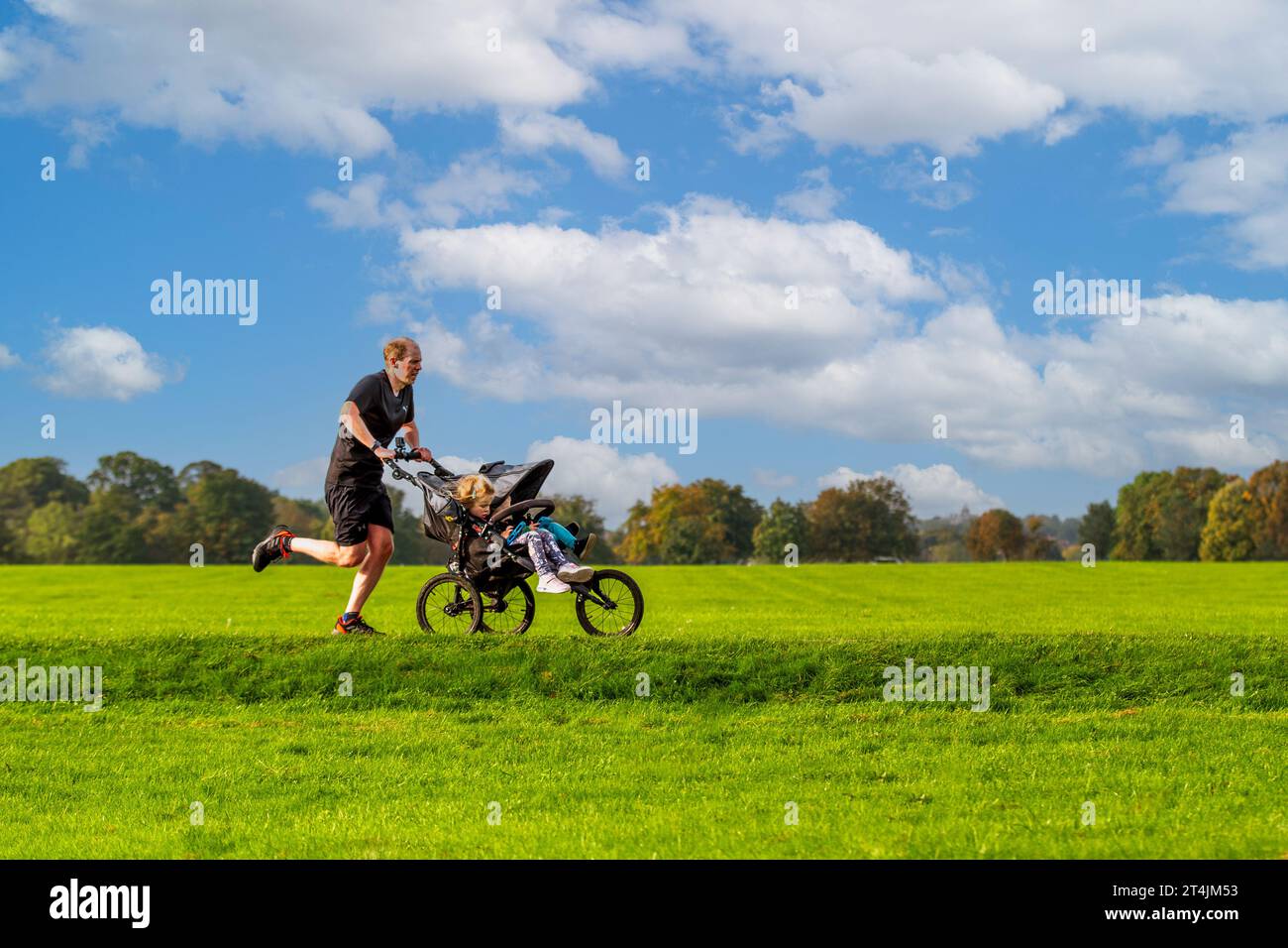 HARROGATE, REGNO UNITO - 30 SETTEMBRE 2023. Vista del profilo di un padre che corre nel parco in una giornata di sole e spinge i suoi figli su un passeggino in una Parkrun Foto Stock