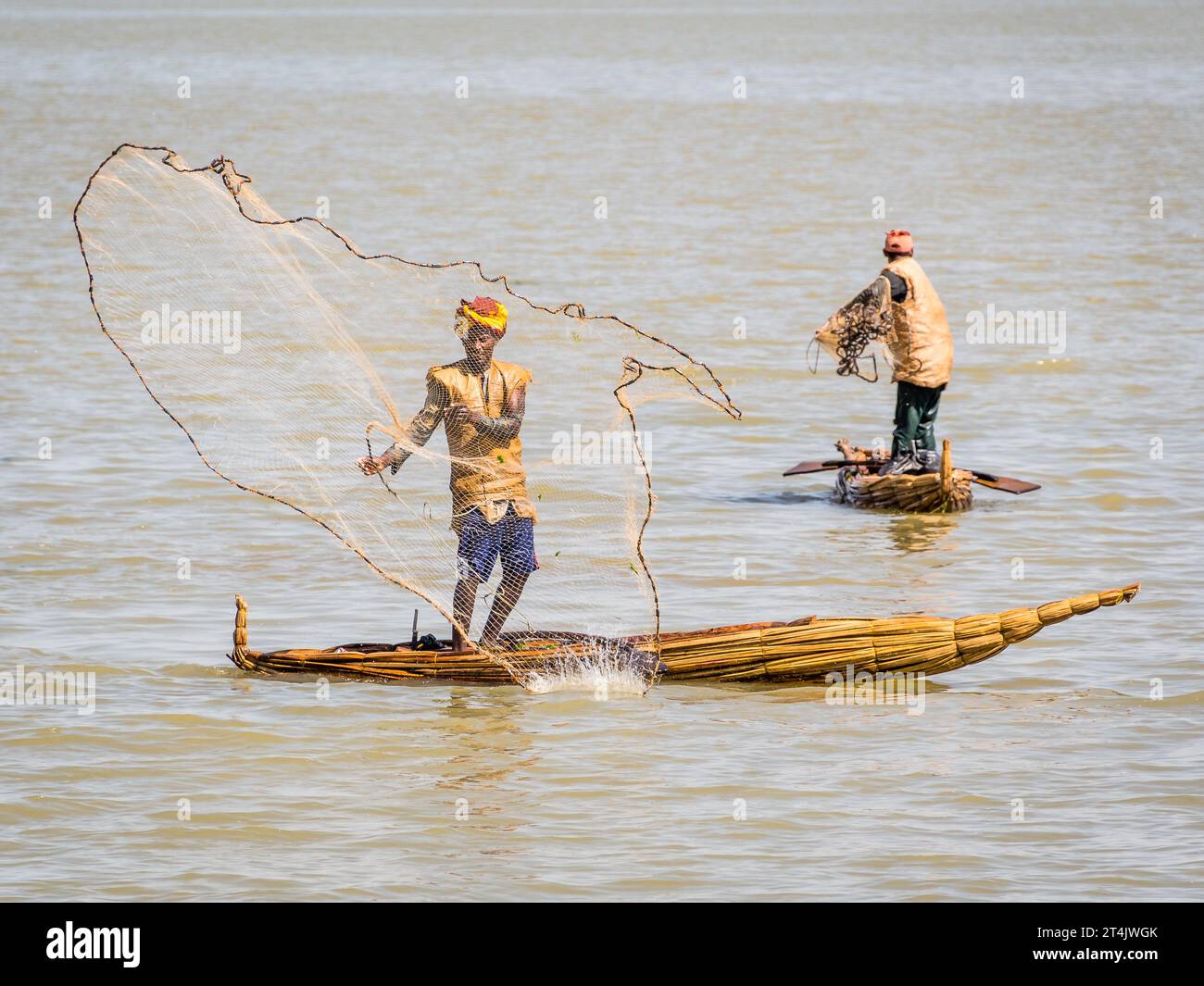 Un pescatore in piedi su una barca tradizionale che getta una rete da pesca Foto Stock