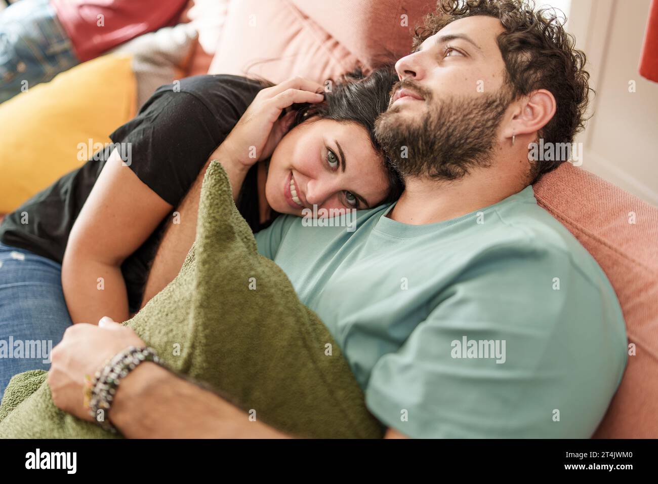 Una donna con un caldo sorriso si appoggia sul petto del partner, condividendo un momento intimo e rilassato insieme su un divano, circondato da morbidi cuscini, e sfoggiando un'esperienza unica Foto Stock