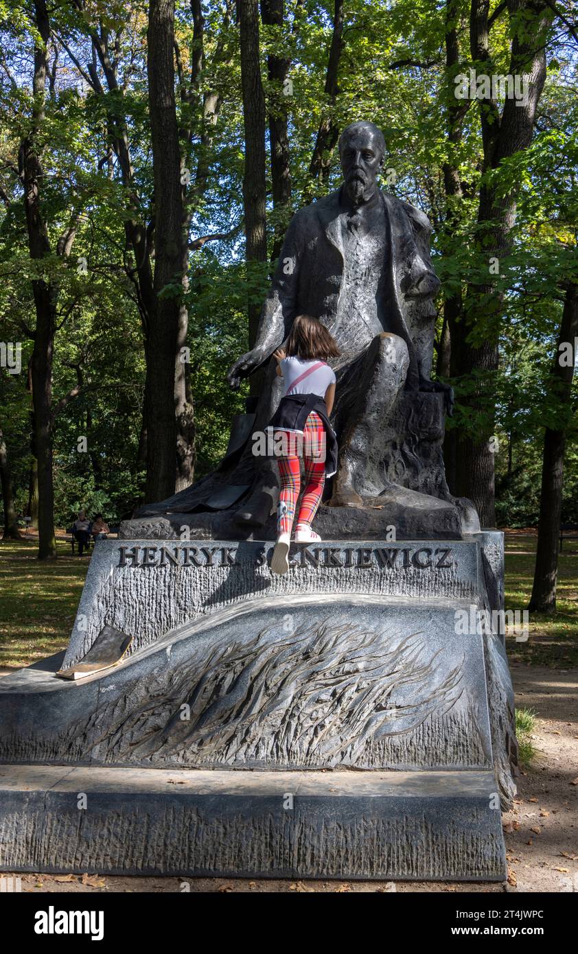Giovane ragazza che gioca sul Monumento a Henryk Sienkiewicz di Kazimierz Gustaw Zemła, Parco Lazienki, Varsavia, Polonia Foto Stock