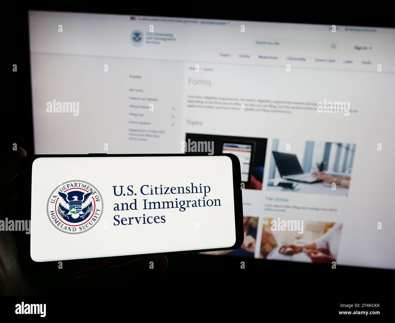 Persona che possiede uno smartphone con il sigillo dell'agenzia statunitense Citizenship and Immigration Services (USCIS) davanti al sito Web. Concentrarsi sul display del telefono. Foto Stock