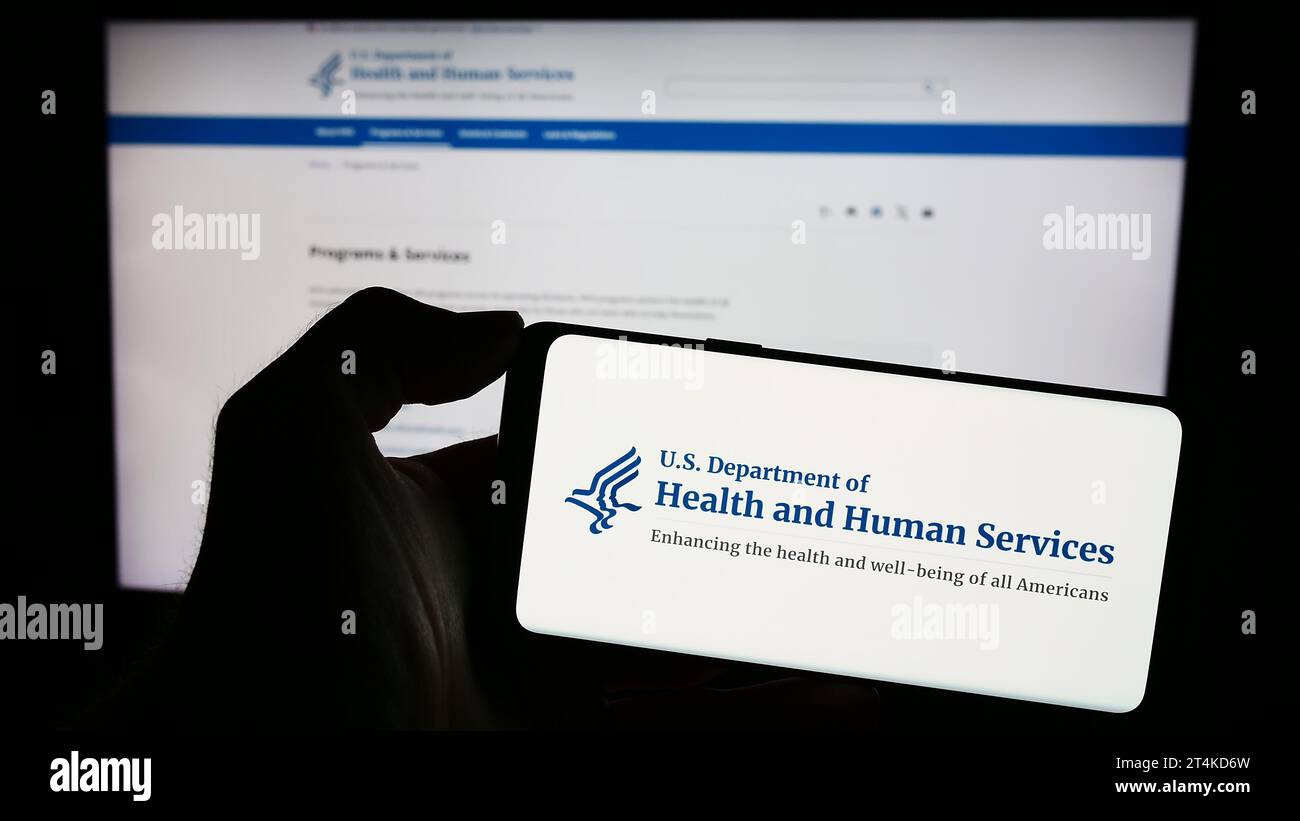 Persona in possesso di un telefono cellulare con il logo del Dipartimento della salute e dei servizi umani (HHS) degli Stati Uniti davanti alla pagina web. Concentrarsi sul display del telefono. Foto Stock