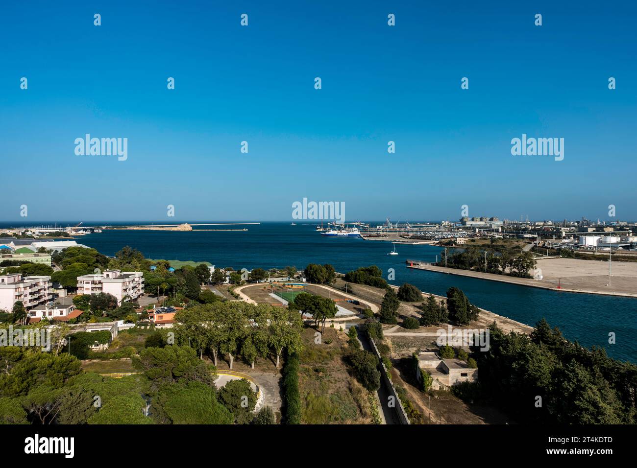 Vista aerea di Brindisi, Italia, che mostra il mare Adriatico, il porto, il terminal dei traghetti, gli edifici residenziali e gli alberi sotto un cielo azzurro. Foto Stock