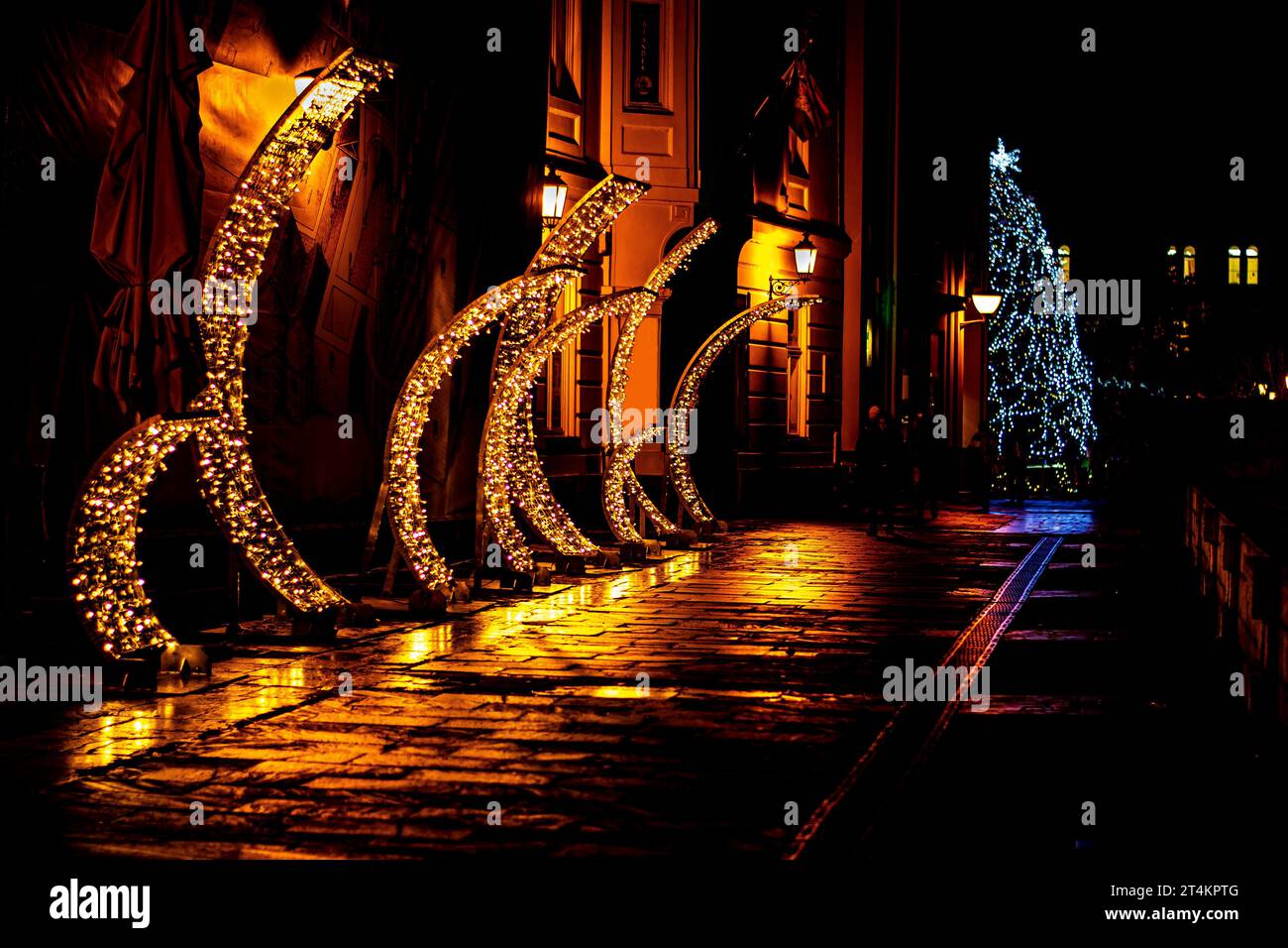 Una serie di luci di Natale gialle su una strada notturna della città dopo la pioggia Foto Stock