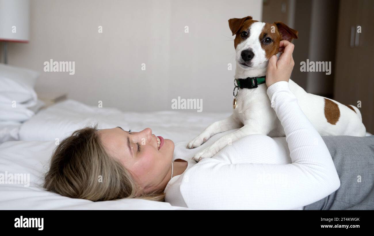 Hotel che accetta cani. Una ragazza e un cane dormono in un letto bianco a casa. Felice cane di razza mista in un letto di lusso. Gli animali domestici sono ammessi in hotel. Cane sul Foto Stock