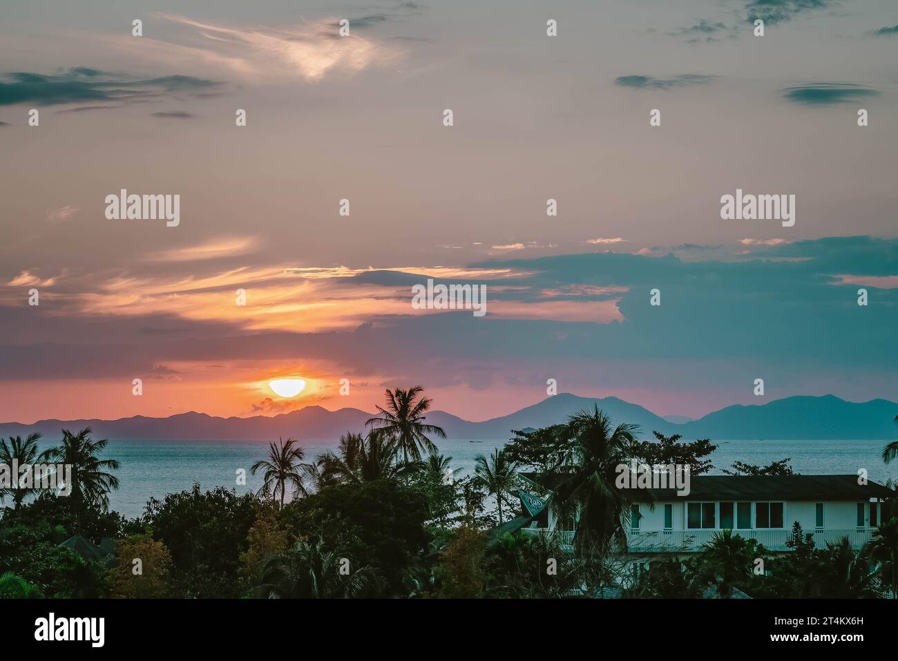 Tramonto panoramico con luce dorata rosa. Mezzo sole nascosto tra nuvole sopra le montagne. Vista ravvicinata su palme, mare e montagne all'orizzonte. Ao Nang Thailandia Foto Stock