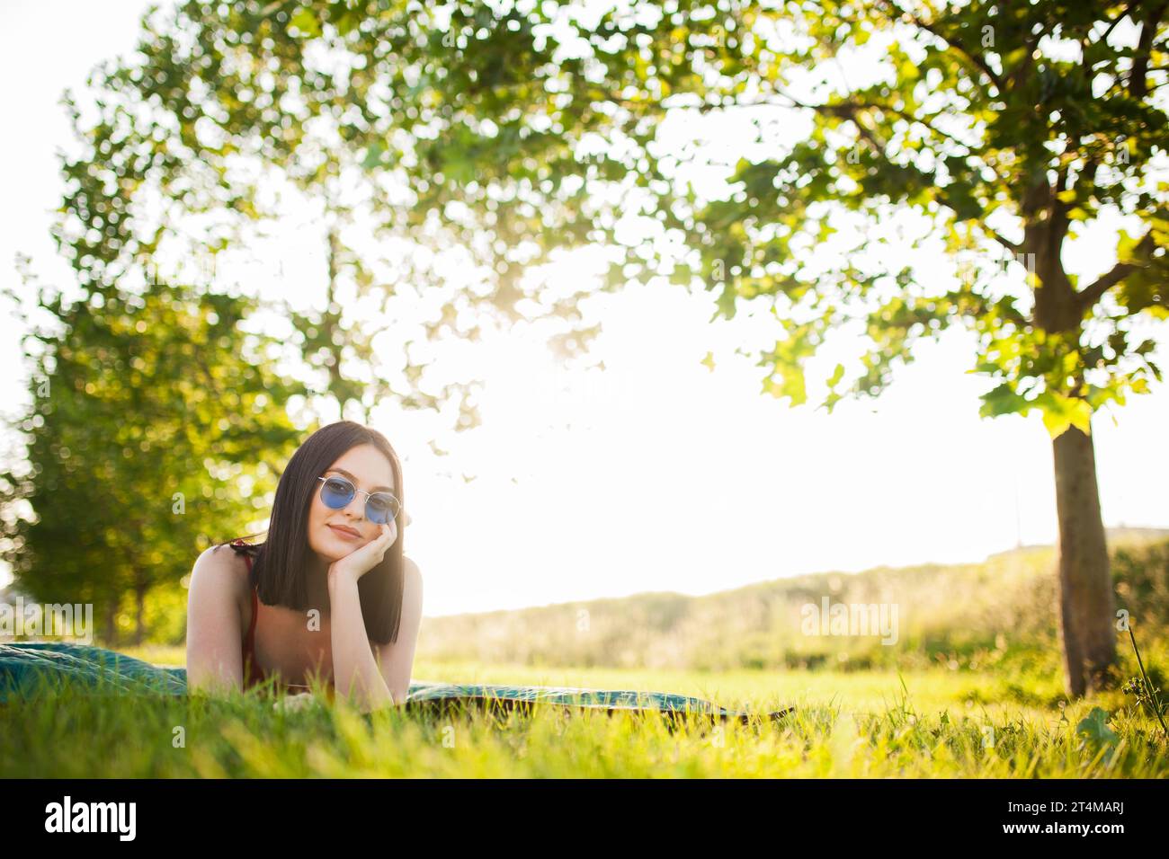 Bellissima ragazza dai capelli scuri con occhiali da sole sdraiata su un prato nel parco. Foto Stock