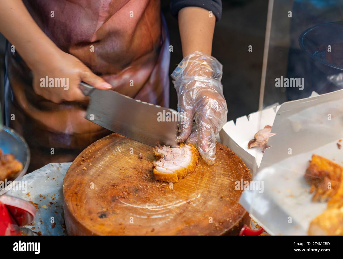 Donna che trita la pancia croccante di maiale chashu su un tagliere di legno nel mercato del cibo di strada. Foto Stock