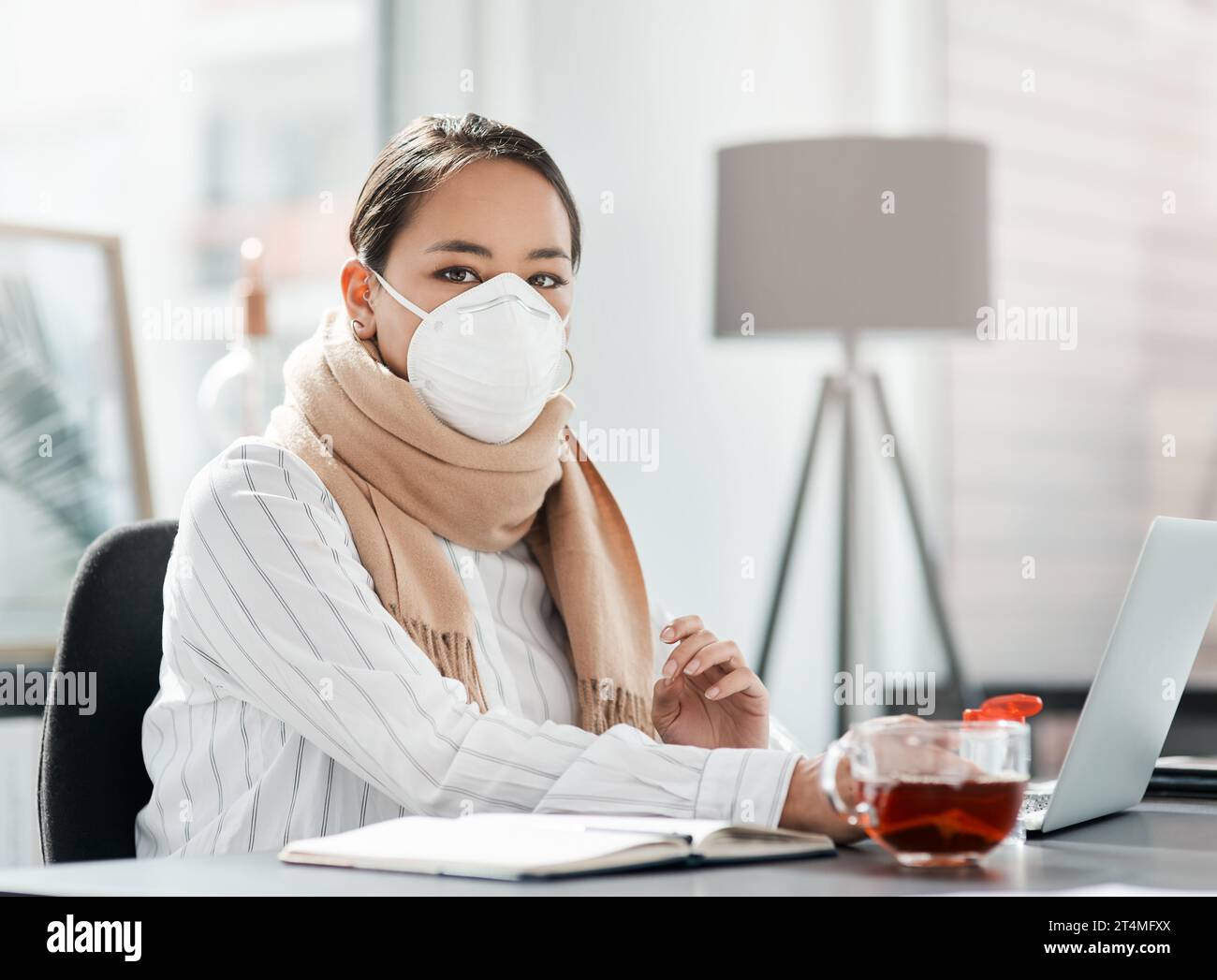 Facciamo quello che dobbiamo per continuare. una giovane donna d'affari mascherata che usa un notebook alla sua scrivania in un ufficio moderno. Foto Stock