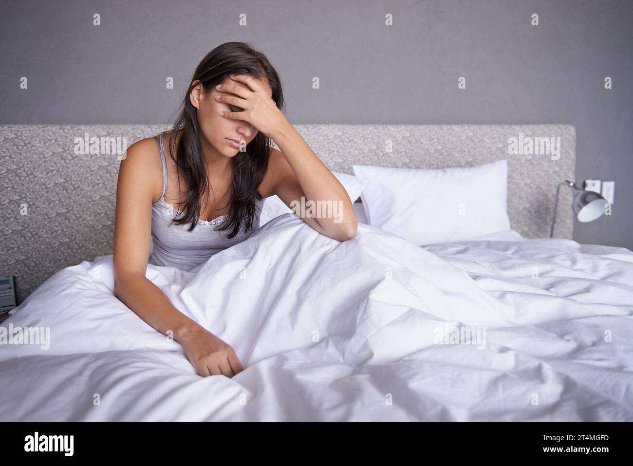 Ho iniziato lentamente stamattina. una giovane donna attraente seduta sul suo letto che sembra infelice. Foto Stock