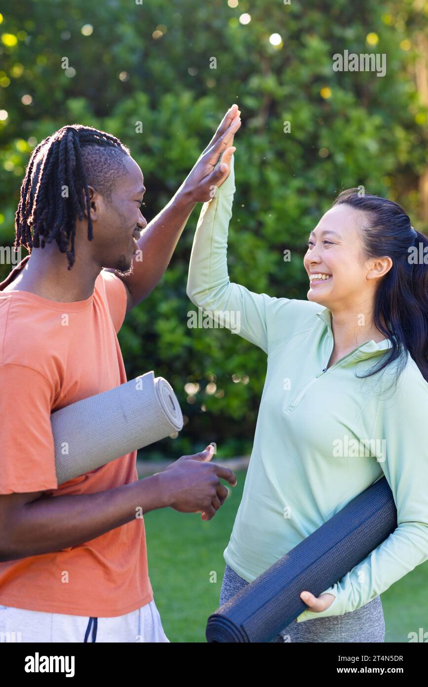 Coppia allegra e diversificata con stuoie da yoga in giardino soleggiato Foto Stock