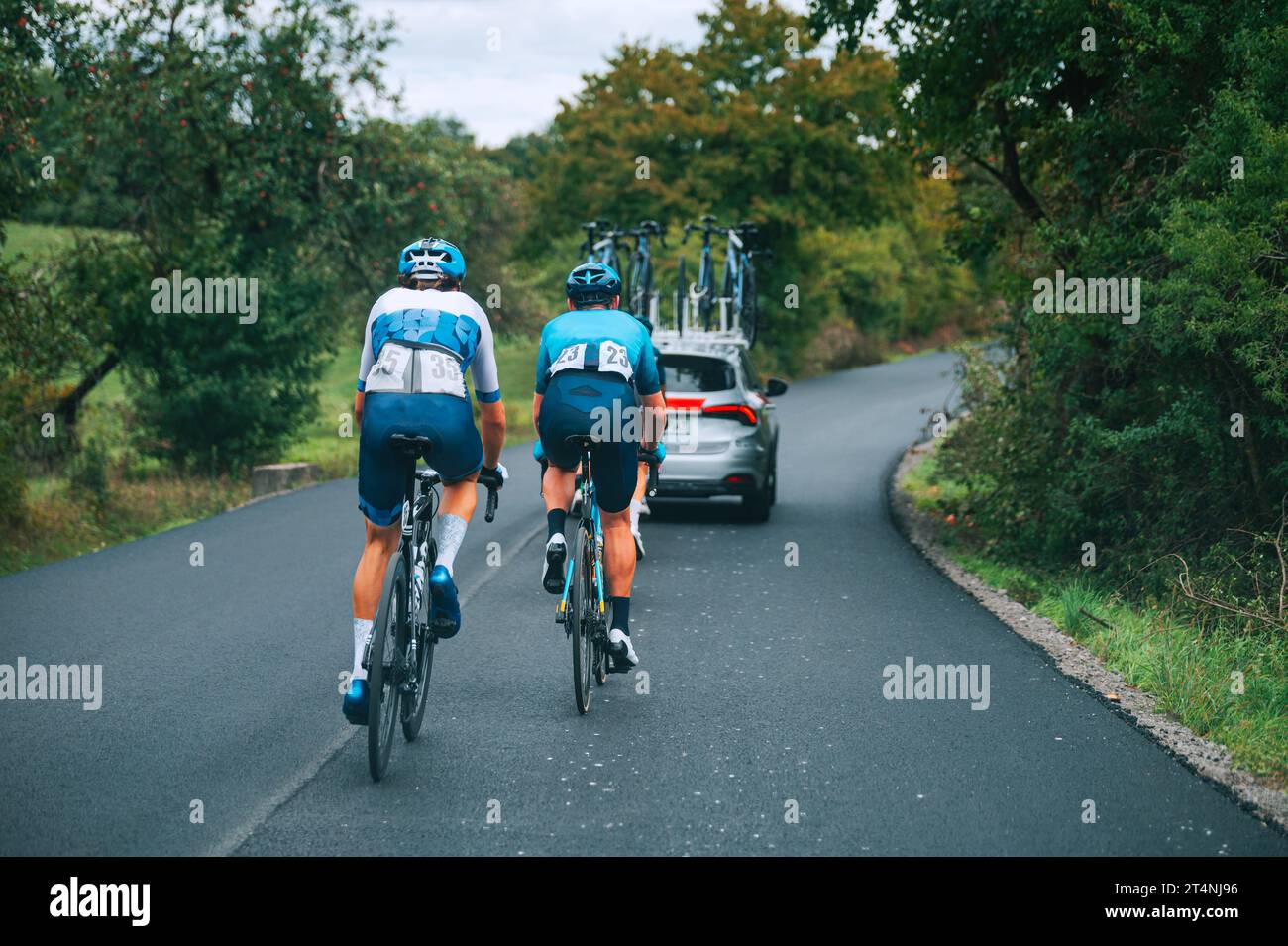 Gara di ciclisti professionisti. Due ciclisti dietro il gruppo in un convoglio di auto sulla strada. Cycling Road Race, preparazione per la gara Tour in Francia. Foto Stock