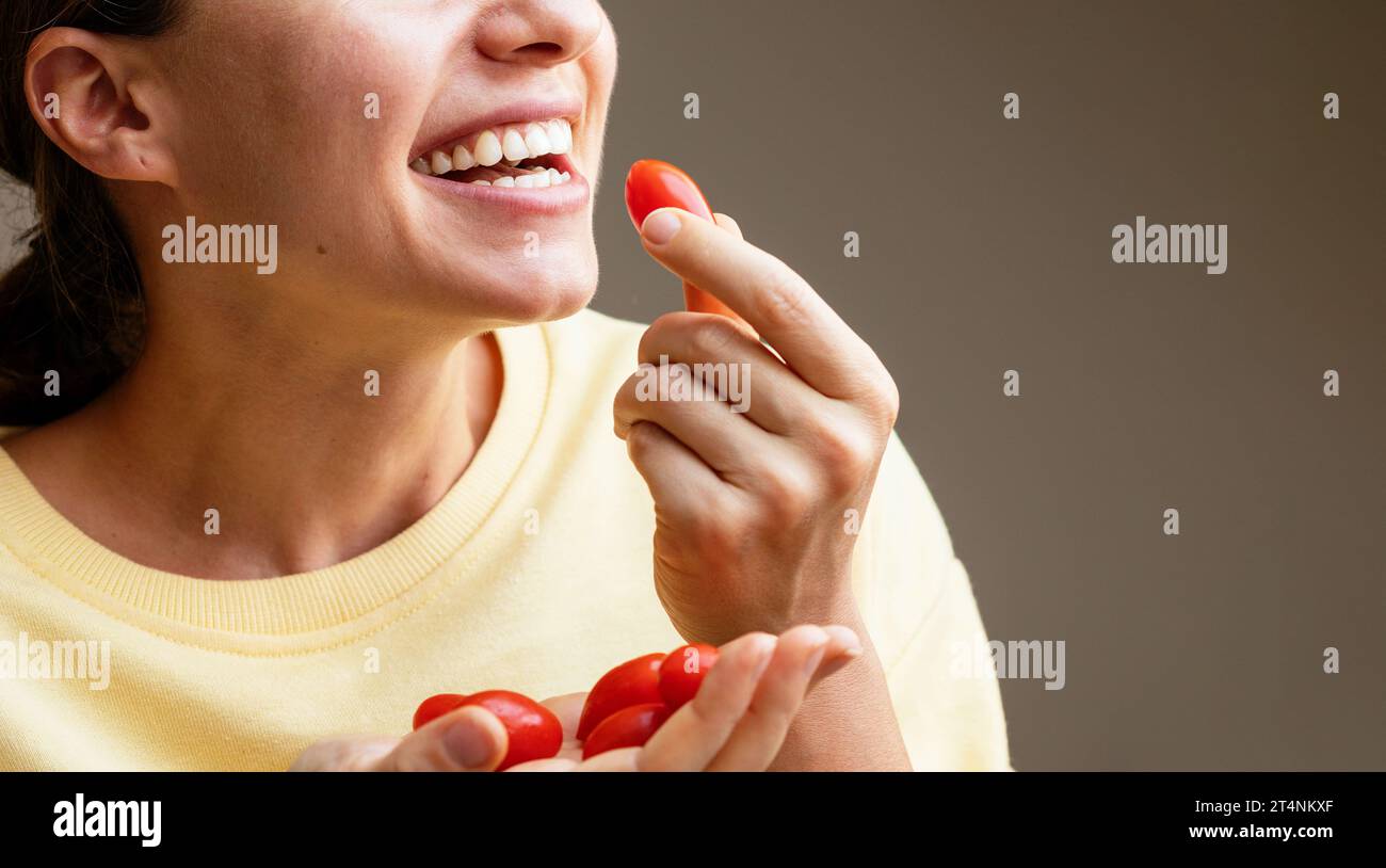 Giovane donna felice che mangia pomodori a bacca rossa. La femmina mangia pomodori ciliegini. Foto Stock