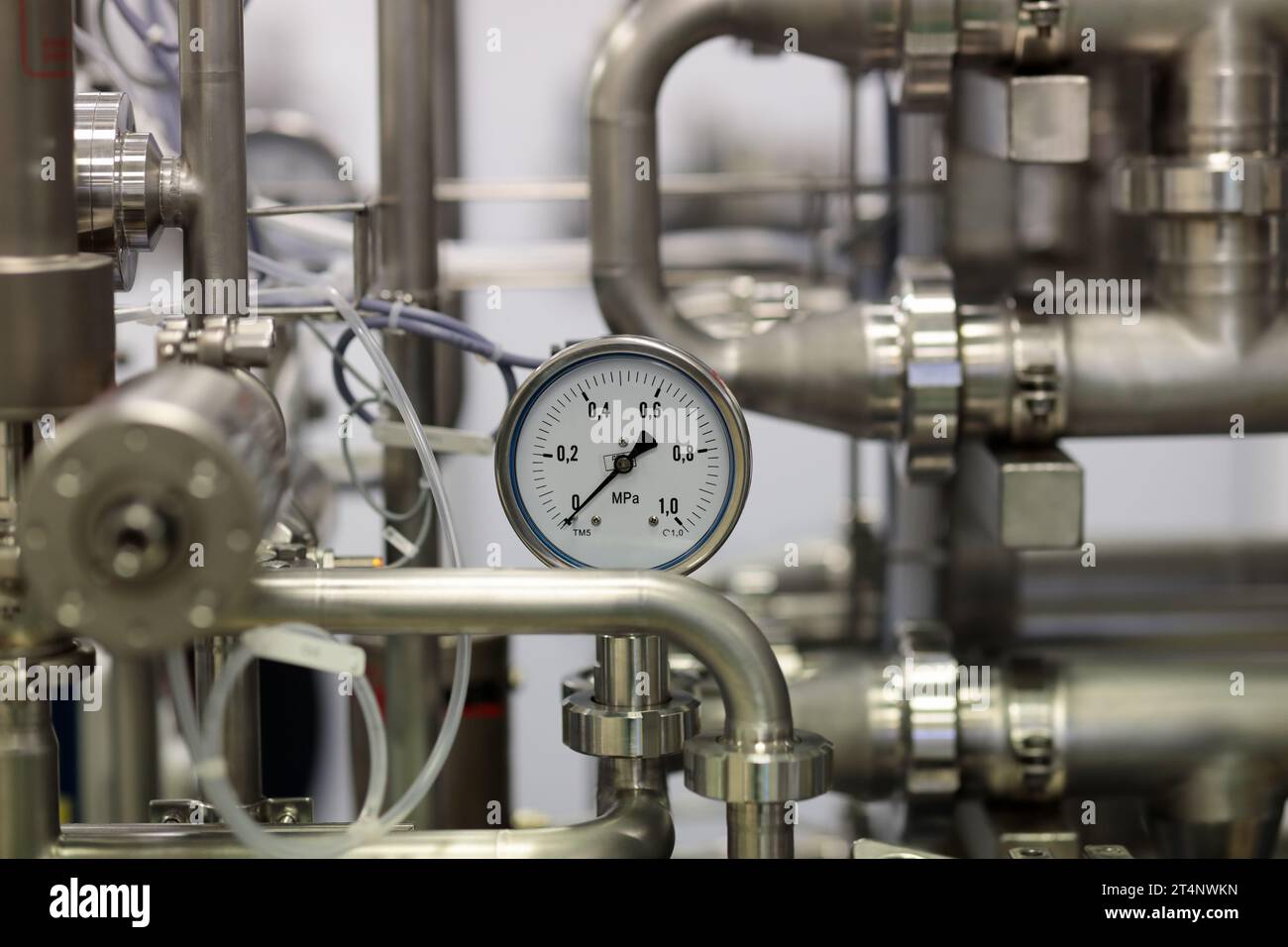 Primo piano dei tubi in acciaio inox e del manometro. Apparecchiature industriali in acciaio inox. Messa a fuoco selettiva. Foto Stock