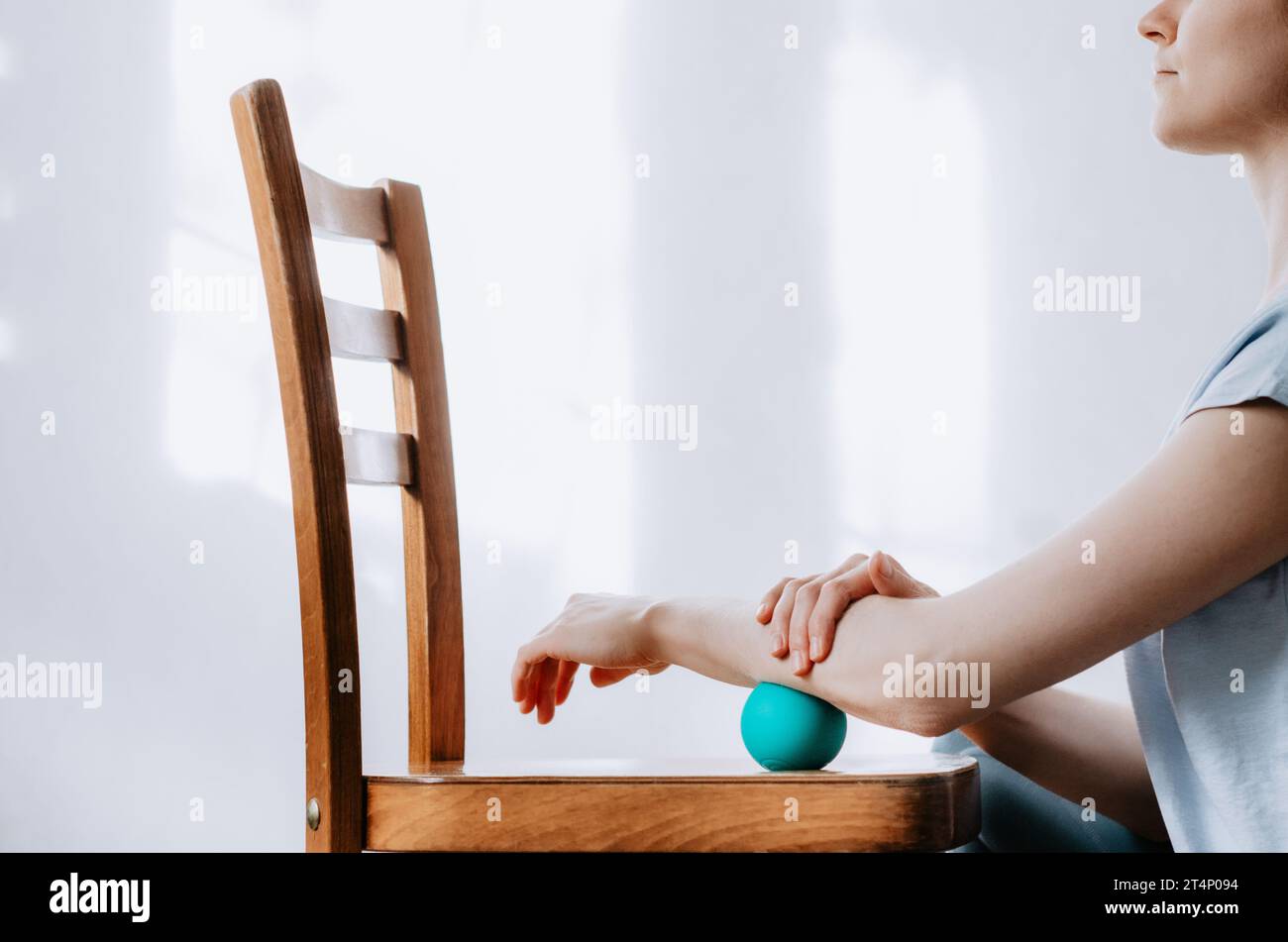 Donna che fa massaggio all'avambraccio con palla terapeutica usando la sedia Foto Stock
