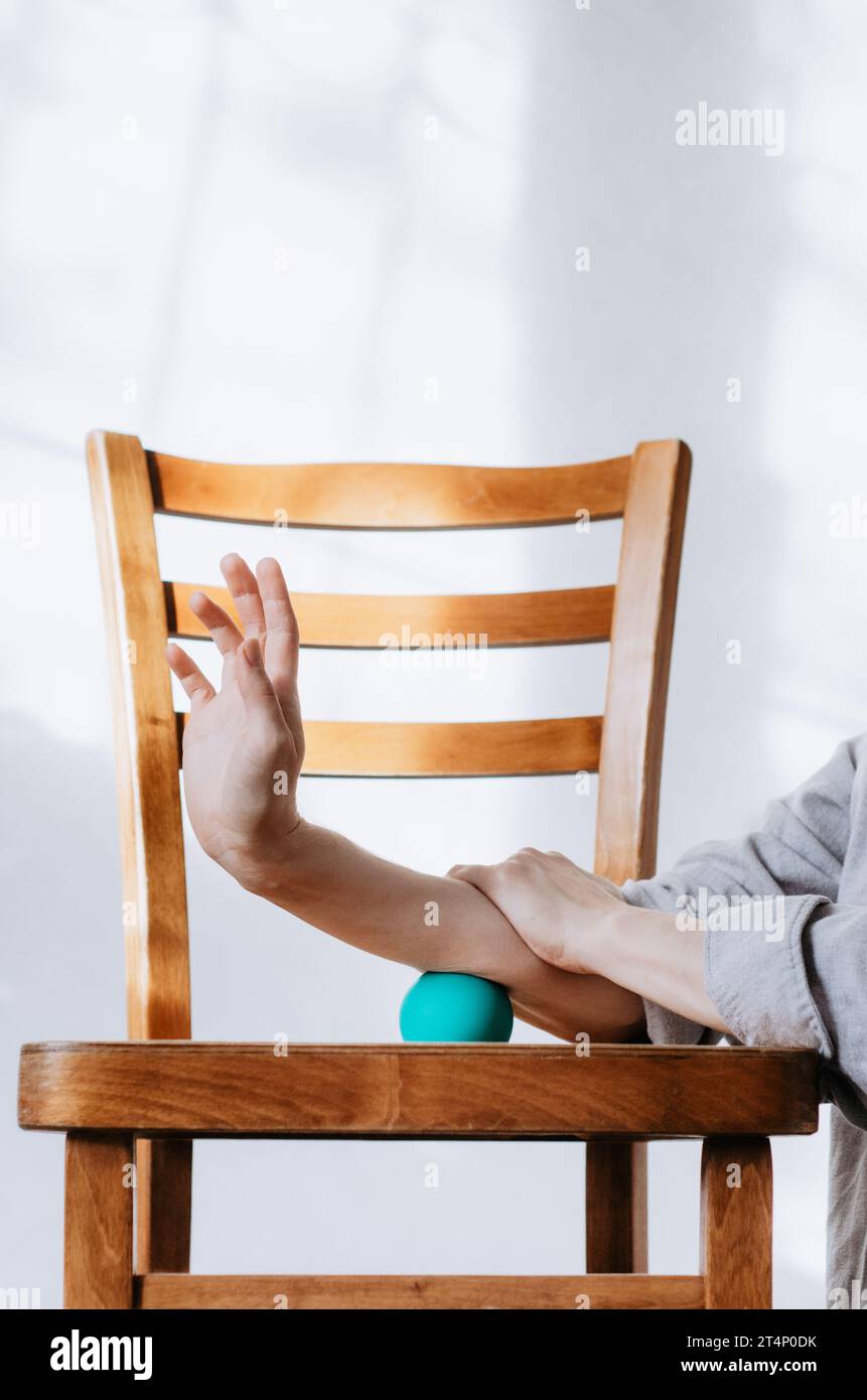Donna che fa massaggio all'avambraccio con palla terapeutica usando la sedia Foto Stock