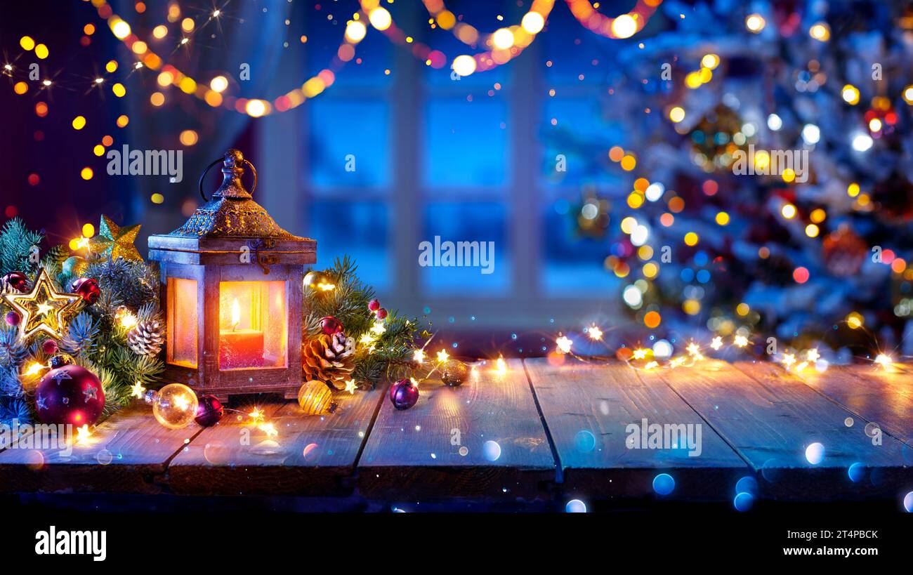 Lanterna e albero di Natale che si illuminano sul tavolo con decorazioni e luci a corda - effetto bokeh e scintillante sullo sfondo Foto Stock