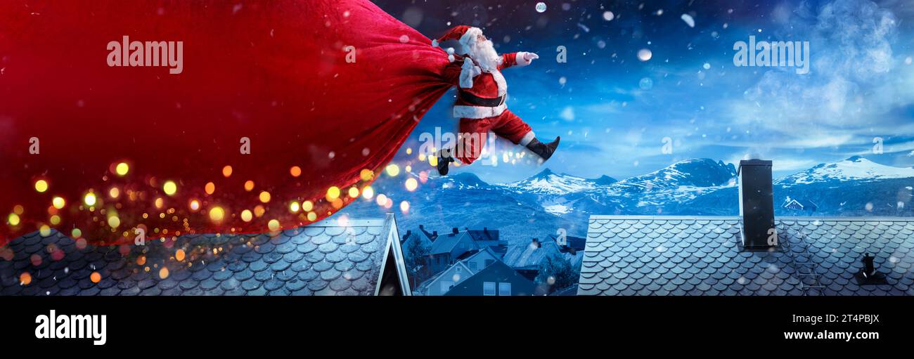 Babbo Natale con Big Bag Rossa che salta sui tetti nel paesaggio invernale innevato - consegna veloce presente Foto Stock