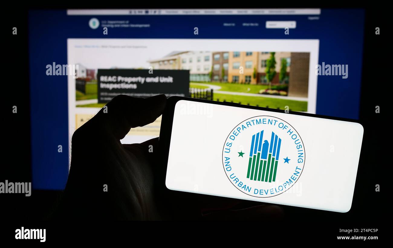 Persona in possesso di un cellulare con il logo dell'American Department of Housing and Urban Development (HUD) davanti alla pagina web. Concentrarsi sul display del telefono. Foto Stock