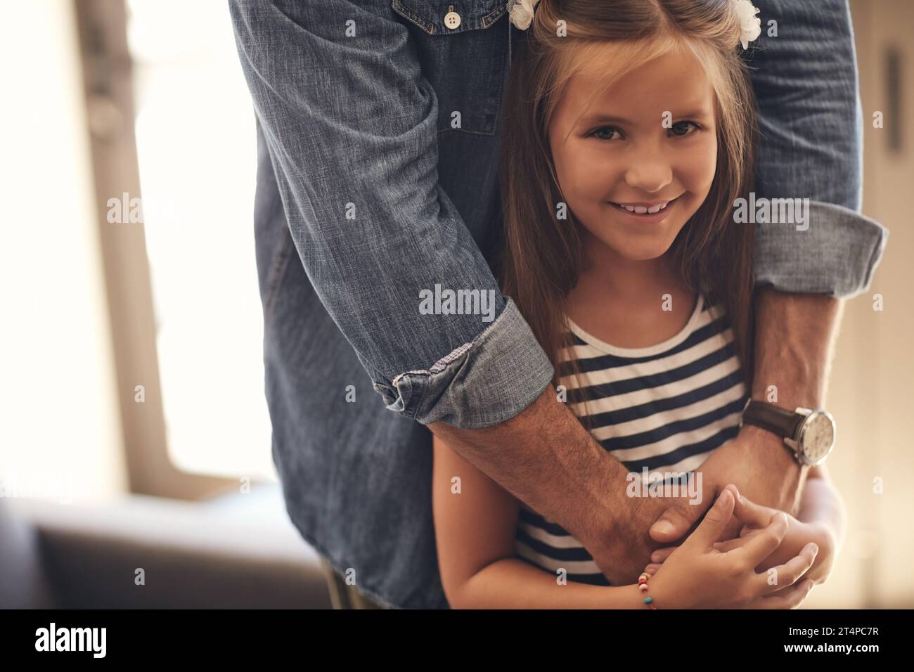 Papà sempre lì per dimostrare che le importa. Ritratto di una bambina adorabile in piedi con le braccia di suo padre intorno a lei a casa. Foto Stock