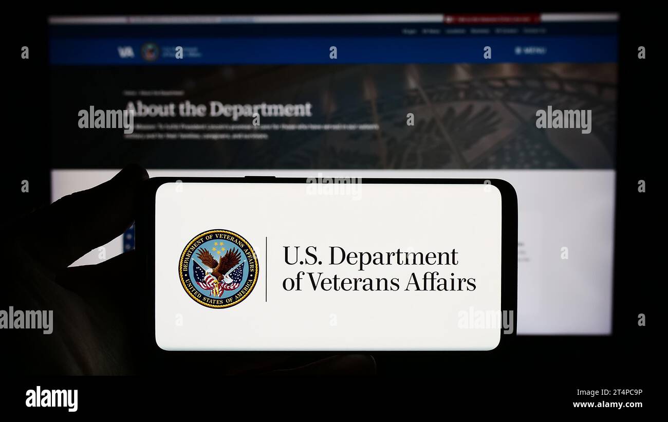Persona che tiene lo smartphone con il sigillo del Dipartimento dei Veterani degli Stati Uniti (va) davanti al sito Web. Concentrarsi sul display del telefono. Foto Stock