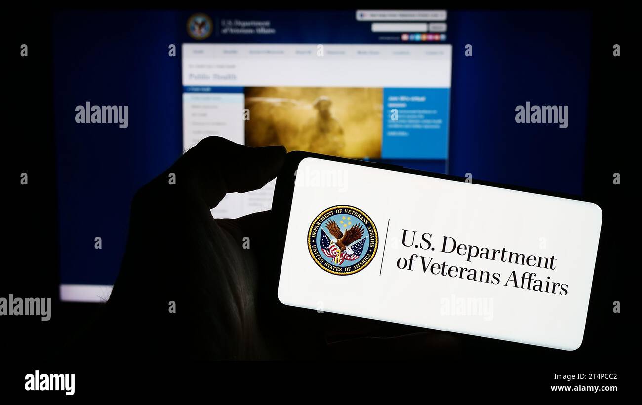 Persona in possesso di un cellulare con il sigillo del Dipartimento dei Veterani degli Stati Uniti (va) davanti alla pagina Web. Concentrarsi sul display del telefono. Foto Stock