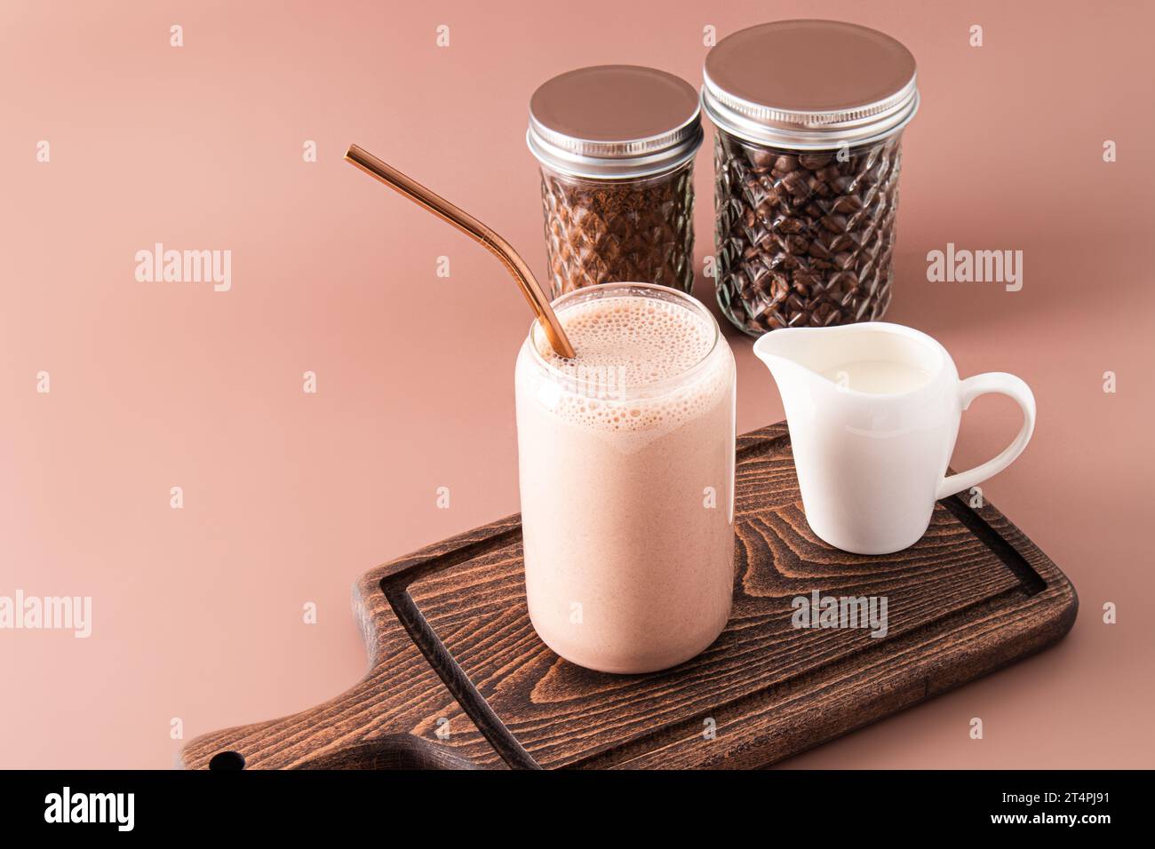 Frullato o caffè appena fatto con latte in un moderno bicchiere a forma di barattolo di birra su un tagliere di legno. Vista frontale Foto Stock