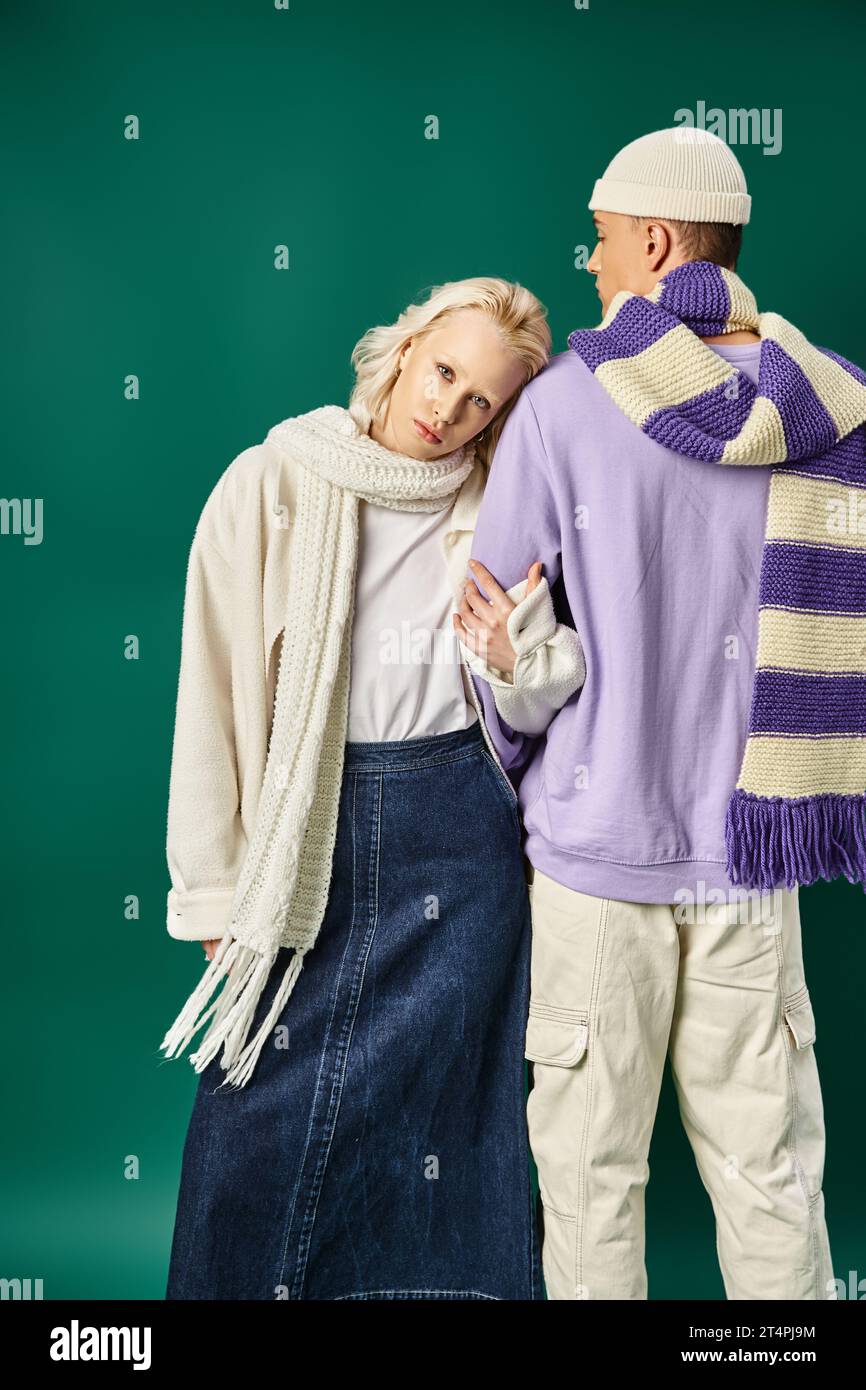 donna bionda con un elegante abbigliamento invernale che mette la testa a spalla di un giovane uomo sullo sfondo turchese Foto Stock