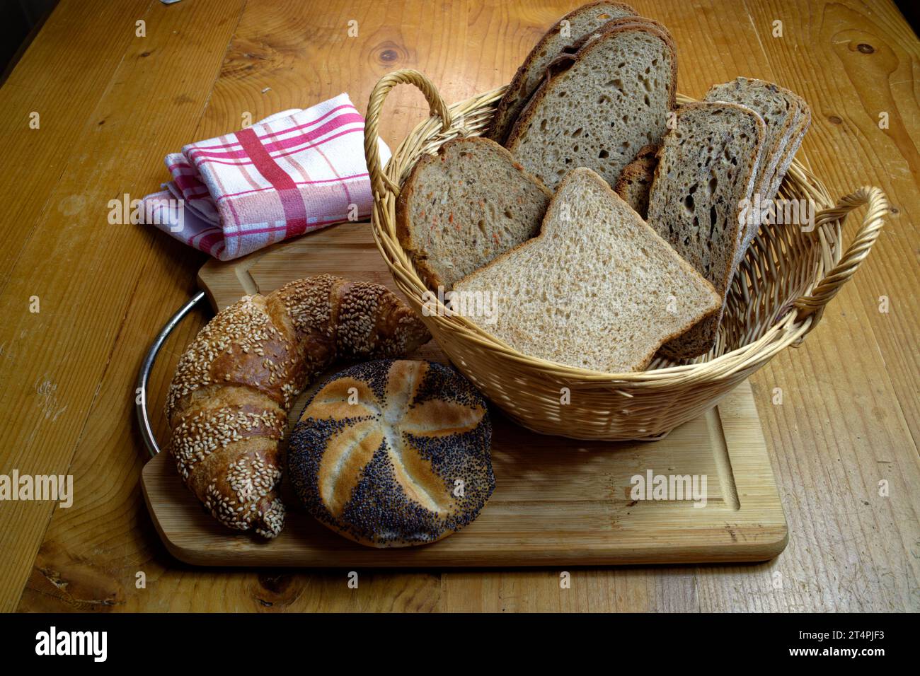 Cestino con diversi tipi di pane, croissant di sesamo e panini di semi di papavero su una tavola di legno Foto Stock
