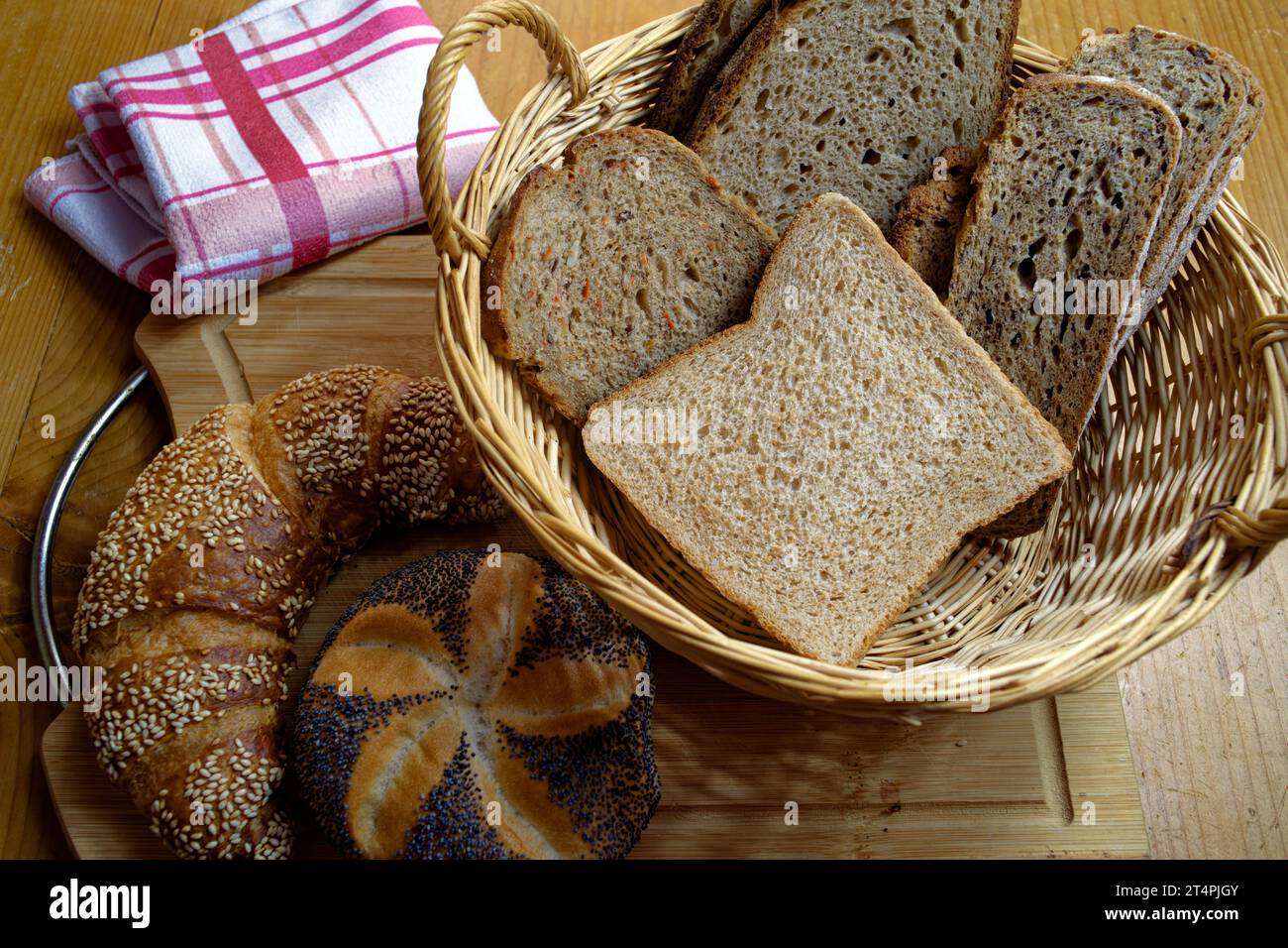 Cestino con diversi tipi di pane, croissant di sesamo e panini di semi di papavero su una tavola di legno Foto Stock