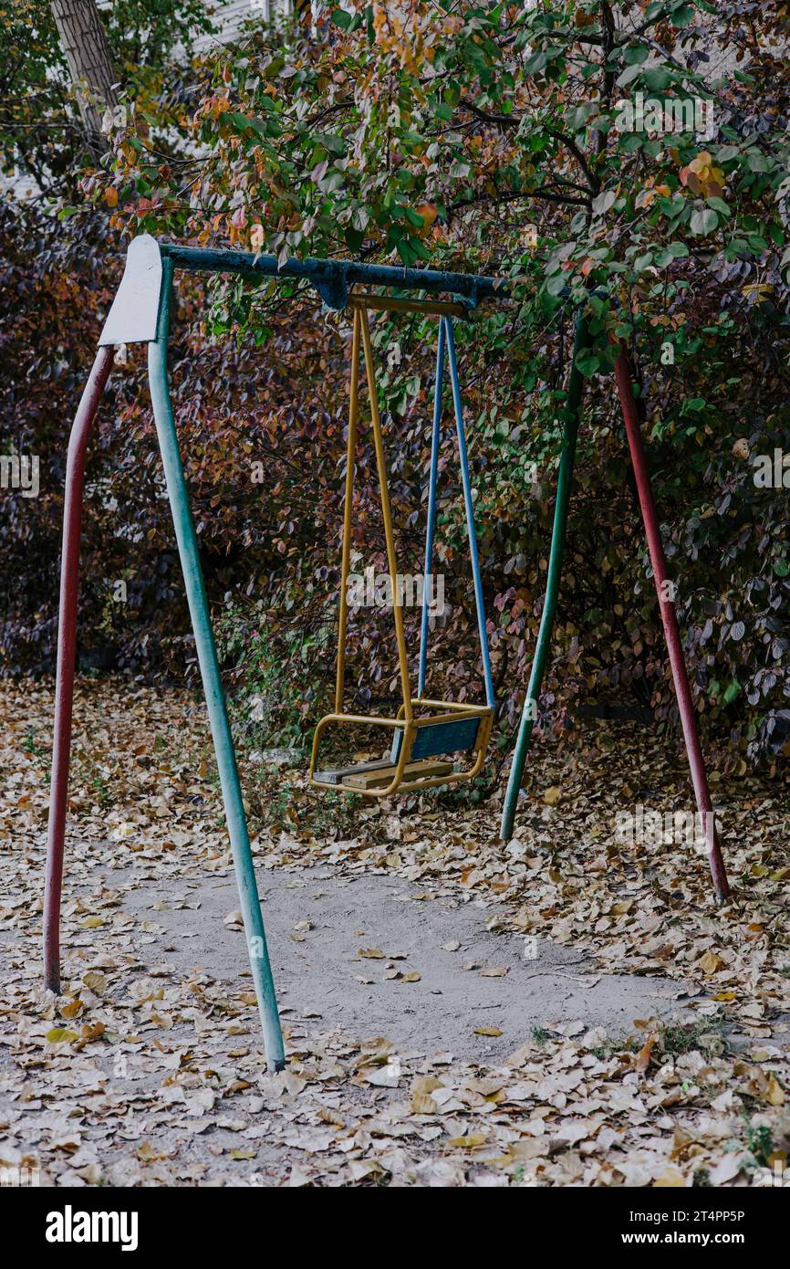 Un vecchio altalena su un parco giochi per bambini realizzato con struttura metallica. Cortile sovietico nel fogliame autunnale. Elementi di gioco non sicuri obsoleti Foto Stock